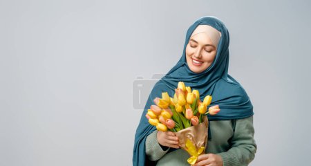 Téléchargez les photos : Belle jeune femme avec des fleurs jaunes dans les mains sur fond de mur gris. - en image libre de droit