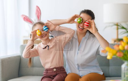 Photo for Happy holiday! Mother and her daughter with painting eggs. Family celebrating Easter. Cute little child girl is wearing bunny ears. - Royalty Free Image