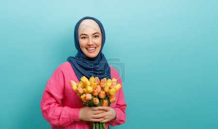 Foto de Hermosa joven con flores amarillas en las manos sobre fondo de pared de color verde azulado. - Imagen libre de derechos