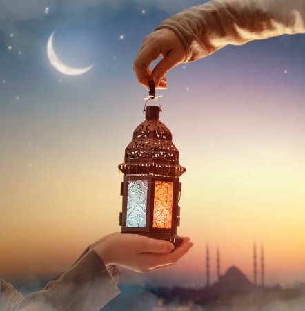 Téléchargez les photos : Lanterne arabe ornementale avec bougie allumée à la main. Carte de vœux festive, invitation pour le mois saint musulman Ramadan Kareem. - en image libre de droit