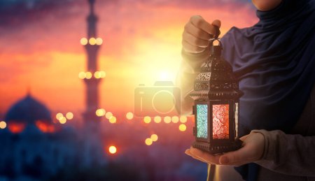 Téléchargez les photos : Femme tient lanterne arabe ornementale avec une bougie allumée qui brille sur le fond de la mosquée de nuit. Carte de vœux festive, invitation pour le mois saint musulman Ramadan Kareem. - en image libre de droit