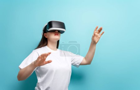 Metaverse technology concept. Woman with VR virtual reality goggles on light blue wall background. Futuristic lifestyle.