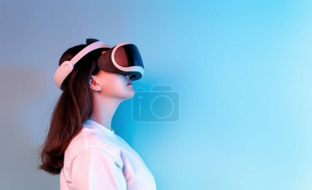 Téléchargez les photos : Concept de technologie Metaverse. Femme avec VR lunettes de réalité virtuelle sur fond de mur bleu clair. Style de vie futuriste. - en image libre de droit