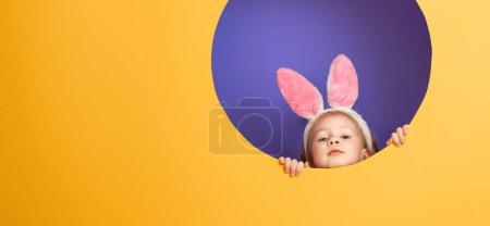 Foto de Lindo niño pequeño con orejas de conejo en el día de Pascua. Chica sobre fondo púrpura brillante y amarillo. - Imagen libre de derechos