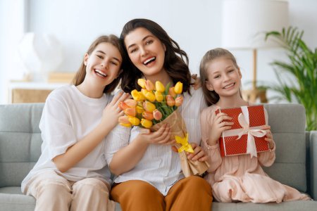 Photo for Happy mother's day. Children daughters are congratulating mom and giving her flowers. Mum and girls smiling and hugging. Family holiday and togetherness. - Royalty Free Image