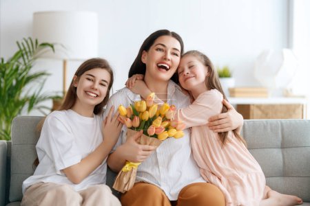 Téléchargez les photos : Bonne fête des mères. Les filles des enfants félicitent maman et lui donnent des fleurs. Maman et les filles souriant et étreignant. Vacances en famille et convivialité. - en image libre de droit