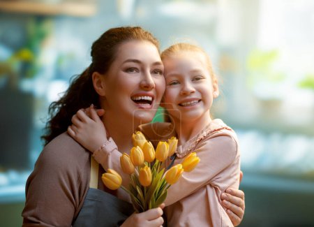 Téléchargez les photos : Bonne fête des mères. Fille enfant félicite maman et lui donne des fleurs. Maman et fille souriant et étreignant. Vacances en famille et convivialité. - en image libre de droit