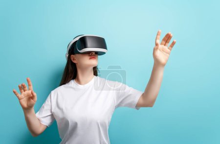 Foto de Concepto de tecnología metaversa. Mujer con gafas de realidad virtual VR sobre fondo de pared azul claro. Estilo de vida futurista. - Imagen libre de derechos