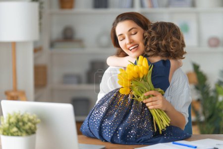 Téléchargez les photos : Bonne fête des mères. Fille enfant félicitant maman et lui donnant des fleurs. Maman et fille souriant et étreignant. Vacances en famille et convivialité. - en image libre de droit