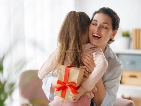 Foto de Feliz día de la madre. La hija del niño felicita a mamá y le da su caja de regalo. Mamá y niña sonriendo y abrazándose. Vacaciones familiares y unión. - Imagen libre de derechos
