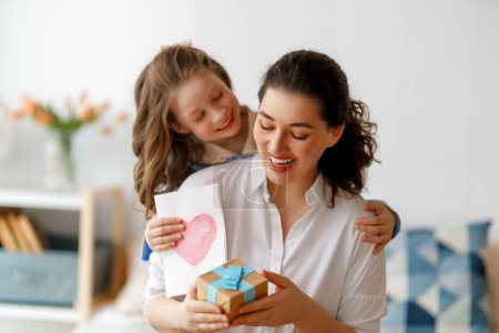 Photo for Happy mother's day. Child daughter is congratulating mom and giving her postcard. Mum and girl smiling and hugging. Family holiday and togetherness. - Royalty Free Image