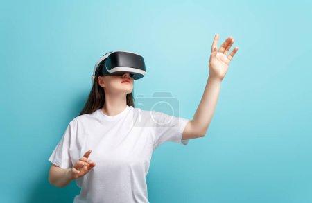 Metaverse technology concept. Woman with VR virtual reality goggles on light blue wall background. Futuristic lifestyle.