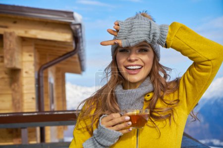 Foto de Mujer bebiendo té caliente en la terraza rústica de madera en la montaña, vista alpina, nieve en las colinas. - Imagen libre de derechos