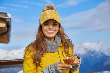 Foto de Mujer bebiendo té caliente en la terraza rústica de madera en la montaña, vista alpina, nieve en las colinas. - Imagen libre de derechos