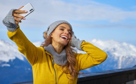 Foto de La tecnología y el concepto de ocio - mujer feliz en invierno sombrero de piel tomando selfie por teléfono inteligente al aire libre - Imagen libre de derechos