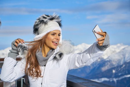 Téléchargez les photos : Concept de technologie et de loisirs - femme heureuse en chapeau de fourrure d'hiver prenant selfie par smartphone à l'extérieur - en image libre de droit