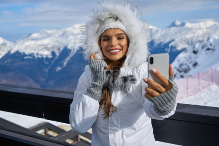 Foto de La tecnología y el concepto de ocio - mujer feliz en invierno sombrero de piel tomando selfie por teléfono inteligente al aire libre - Imagen libre de derechos