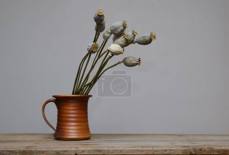 Téléchargez les photos : Têtes de graines de pavot séchées dans un vase en céramique sur table en bois - en image libre de droit