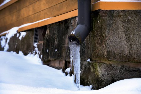 Téléchargez les photos : Drain glacé près de la fondation en pierre d'une vieille maison en hiver - en image libre de droit
