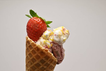 Deliciosas cucharadas de helado de vainilla y bayas en un cono de gofre cubierto con una fresa fresca y hoja de menta sobre un fondo blanco