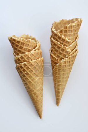 Téléchargez les photos : Deux cônes de gaufres brun doré croustillants se dressent sur un fond blanc uni, prêts à être remplis de délicieuses glaces - en image libre de droit