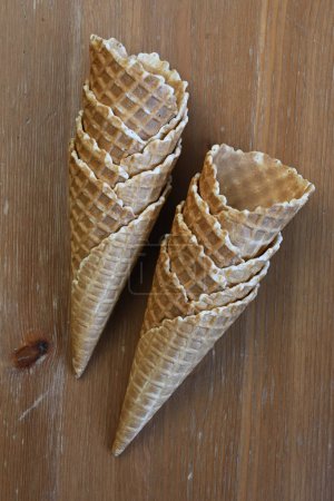 Two crispy golden brown waffle cones stand upright on a wooden table, ready to be filled with delicious ice cream 