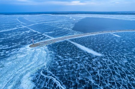 Téléchargez les photos : Vue aérienne d'un phare solitaire dans la mer gelée. Glace bleue gelée dans les fissures, vue sur drone - en image libre de droit