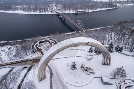 Photo for Aerial drone view. Pedestrian bridge over the frozen Dnieper River in Kiev. Cloudy frosty winter morning, frosty pattern on ice. - Royalty Free Image