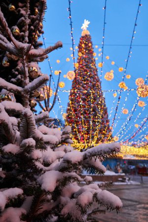 Foto de Gran hermoso árbol de Navidad con decoraciones e iluminaciones en la noche nevada. Año Nuevo y fondo de vacaciones de Navidad. Paisaje festivo invierno ciudad. - Imagen libre de derechos