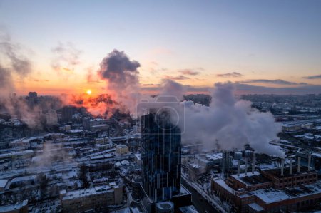 Foto de El humo sale de la tubería de la caldera. Sistema de calefacción central de edificios de apartamentos. Puesta de sol invierno - Imagen libre de derechos