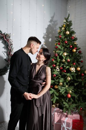 Téléchargez les photos : Jeune doux joli couple amoureux embrasser dans la veille de Noël près de l'arbre avec des cadeaux à la maison en Décembre
. - en image libre de droit