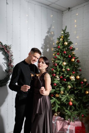 Photo for Young couple in love posing near the Christmas tree and hugging - Royalty Free Image