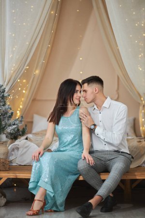 Foto de Joven pareja enamorada sentada cerca del árbol de Navidad y abrazándose - Imagen libre de derechos