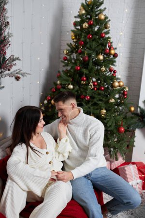Photo for Young couple in love sitting near the Christmas tree and hugging - Royalty Free Image