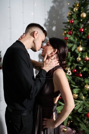 Foto de Joven pareja enamorada de pie cerca del árbol de Navidad y abrazándose - Imagen libre de derechos
