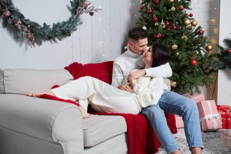 Photo for Young sweet pretty couple in love kissing in christmas eve near tree with gifts at home in december. - Royalty Free Image