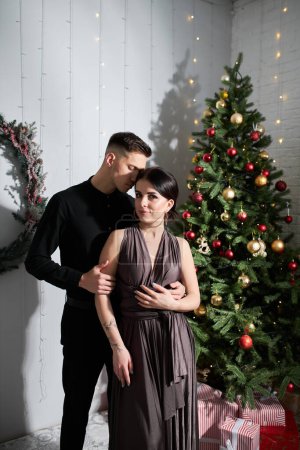 Téléchargez les photos : Beau couple amoureux. Joyeux jeune couple dans des vêtements élégants de soirée. Mode, glamour. Couple câlins à Noël intérieur décoré - en image libre de droit