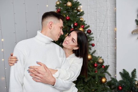 Téléchargez les photos : Jeune doux joli couple amoureux embrasser dans la veille de Noël près de l'arbre avec des cadeaux à la maison en Décembre
. - en image libre de droit
