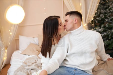 Photo for Young sweet pretty couple in love kissing in christmas eve near tree with gifts at home in december. - Royalty Free Image