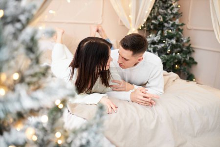 Photo for Young couple in love lying near the Christmas tree and hugging - Royalty Free Image