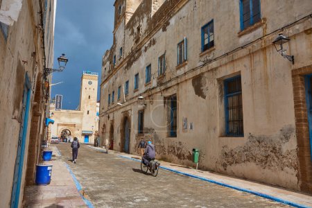 Téléchargez les photos : ESSAOUIRA, MOROCCO. 13 th February, 2017: Ancient walls of the medina , merchants hurrying on business, after the rain - en image libre de droit