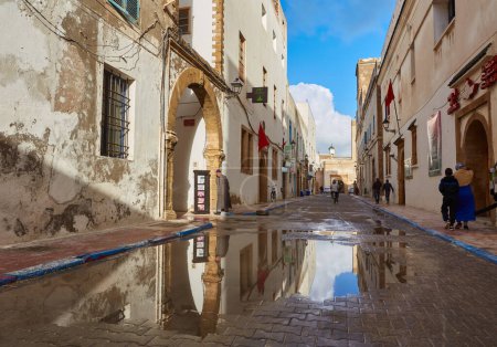 Téléchargez les photos : ESSAOUIRA, MOROCCO. 13 th February, 2017: Ancient walls of the medina, merchants hurrying on business, after the rain - en image libre de droit