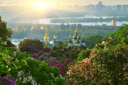 Botanical garden in Kyiv at sunrise. Amazing morning landscape with blossoming lilac, green trees, Dnieper river, city view and rising sun in colorful cloudy sky, Ukraine, Eastern Europe