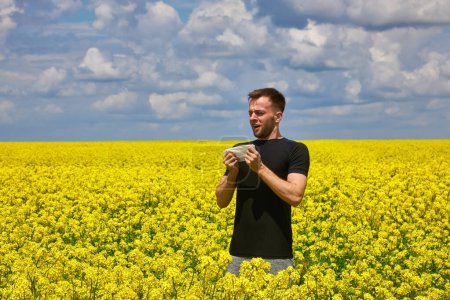 Foto de Hombre joven en el campo de canola amarillo sonándose la nariz y sufriendo de alergia al polen. - Imagen libre de derechos