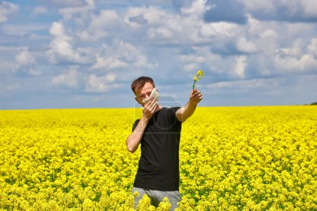 Photo for Young man in yellow canola field blowing his nose and suffering from pollen allergy. - Royalty Free Image