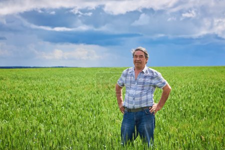 Foto de A Portrait of a happy farmer kneeling down in a wheat field with a beautiful landscape in the background - Imagen libre de derechos