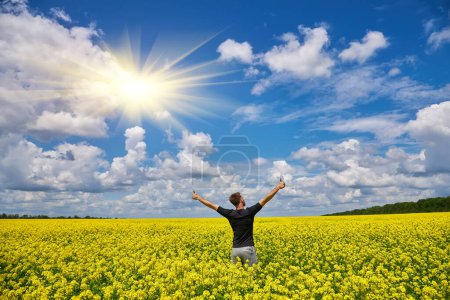 Téléchargez les photos : L'homme heureux se tient dans un champ jaune se réjouissant lève les mains vers le ciel. - en image libre de droit