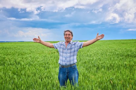 Foto de A Portrait of a happy farmer kneeling down in a wheat field with a beautiful landscape in the background - Imagen libre de derechos