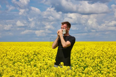Téléchargez les photos : Jeune homme dans le champ de canola jaune se mouchant et souffrant d'allergie au pollen. - en image libre de droit