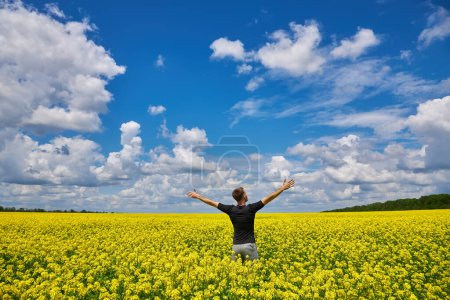 Photo for Happy man stands in a yellow field rejoicing raises his hands to the sky. - Royalty Free Image